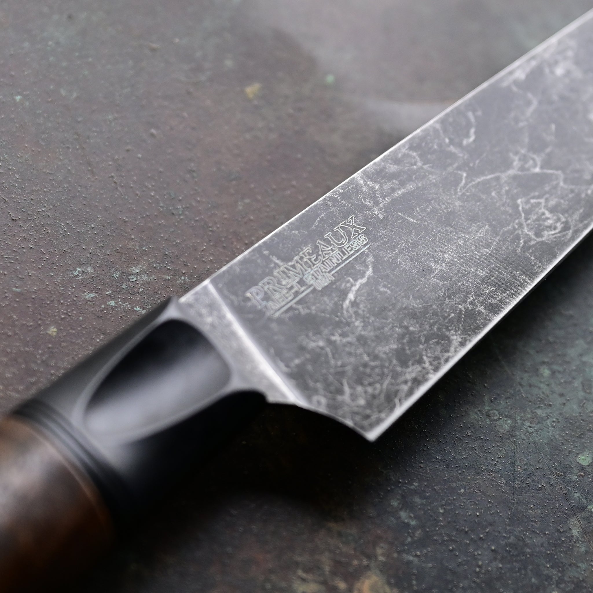 Paring knife with a deep, dark stone wash finish blade on a concrete backdrop, complemented by a black anodized bolster and a rich brown Claro walnut handle, featuring a thin, razor-sharp AEBL blade.